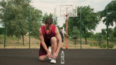 Im-Vordergrund-Kniet-Ein-Männlicher-Basketballspieler-Und-Bindet-Seine-Schnürsenkel
