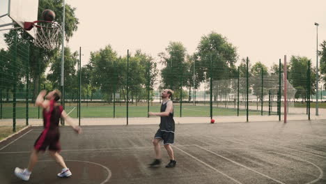 A-Skillfull-Basketball-Player-Dribbling-The-Ball-Between-The-Legs-Against-His-Opposing-Defender,-Throwing-Ball-Into-Outdoor-Basketball-Hoop-And-Giving-High-Five-To-Each-Other