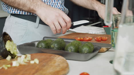 Close-Up-Of-A-Man-Hands-Cutting-Tomatoes-On-A-Wooden-Chopping-Board-In-A-Modern-Kitchen