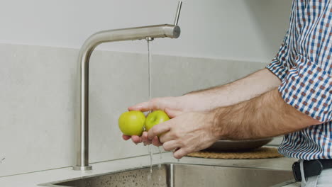 Nahaufnahme-Von-Menschenhänden,-Die-Zwei-Grüne-Äpfel-In-Einer-Modernen-Küchenspüle-Waschen