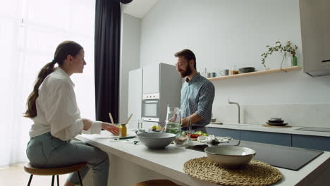 Cheerful-Couple-Chatting-And-Preparing-A-Tasty-Salad-In-A-Modern-Kitchen