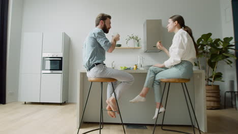Loving-Couple-Chatting-And-Having-Lunch-Together-Sitting-On-Stool-In-A-Modern-Kitchen