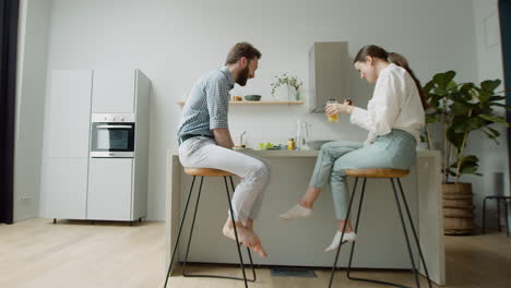 Happy-Couple-Chatting-And-Having-Lunch-Together-Sitting-On-Stool-In-A-Modern-Kitchen