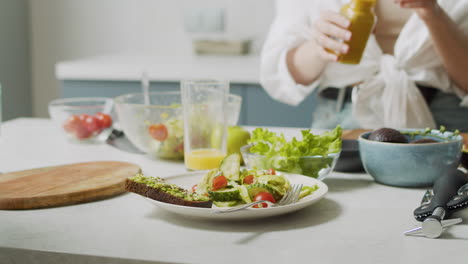 Close-Up-Of-Woman-Hand-Pouring-Honey-Mustard-Dressing-Into-Plate-With-Fresh-Salad-And-Avocado-Toast