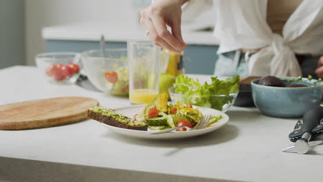 Close-Up-Of-Woman-Hand-Adding-Various-Seeds-Into-Plate-With-Fresh-Salad-And-Avocado-Toast