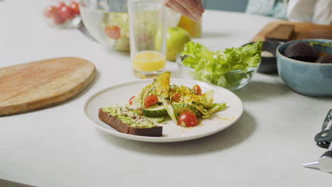 Close-Up-Of-Woman-Hand-Adding-Various-Seeds-Into-Plate-With-Fresh-Salad-And-Avocado-Toast-1