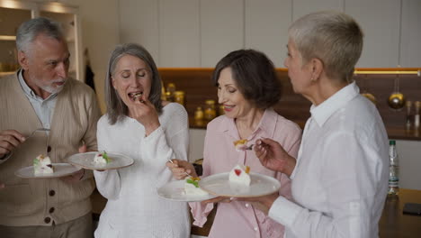Gruppe-Fröhlicher-älterer-Freunde,-Die-Sich-Unterhalten-Und-Ein-Köstliches-Dessert-Essen,-Stehen-In-Einer-Modernen-Küche