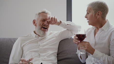 Frau-Und-Mann-Glückliche-ältere-Freunde,-Die-Lachend-Auf-Der-Couch-Sitzen-Und-Ein-Glas-Wein-Trinken