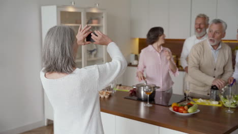 Happy-Senior-Woman-On-A-Video-Call,-While-Her-Friends-Wave-At-The-Camera-While-Laughing-And-Cooking