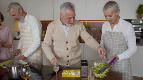 Older-Man-And-Woman-Friends-Cooking-And-Talking-With-Another-Couple-Of-Friends-In-The-Kitchen
