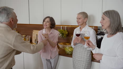 Gruppe-Fröhlicher-älterer-Freunde,-Die-In-Der-Küche-Mit-Gläsern-Wein-Lachen-Und-Anstoßen