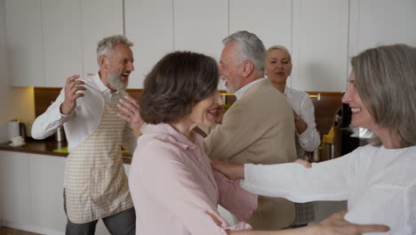 Group-Of-Cheerful-Senior-Friends-Greeting-Each-Other-With-Hugs-In-The-Kitchen