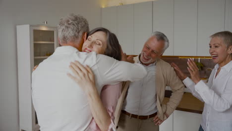 Group-Of-Cheerful-Senior-Friends-Greeting-Each-Other-With-Hugs-In-The-Kitchen-2