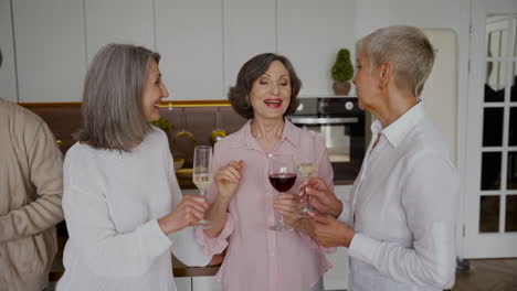 Group-Of-Cheerful-Senior-Women-Friends-Talking,-Laughing-And-Drinking-Wine-In-The-Kitchen
