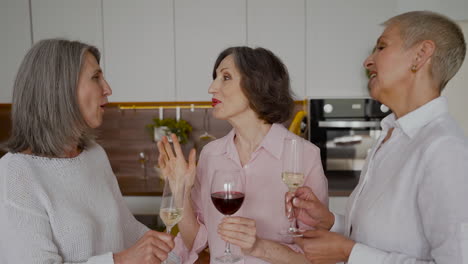 Gruppe-Fröhlicher-älterer-Freundinnen,-Die-In-Der-Küche-Reden,-Lachen-Und-Wein-Trinken-1