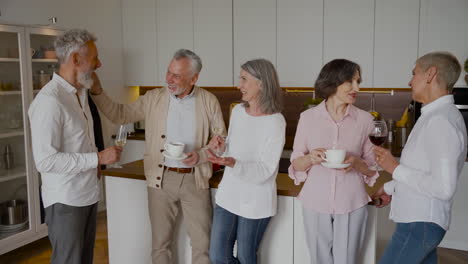 Group-Of-Cheerful-Senior-Friends-Laughing-And-Drinking-Wine-And-Coffee-In-The-Kitchen