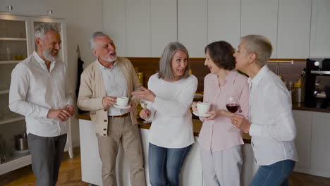 Group-Of-Cheerful-Senior-Friends-Laughing-And-Drinking-Wine-And-Coffee-In-The-Kitchen-1