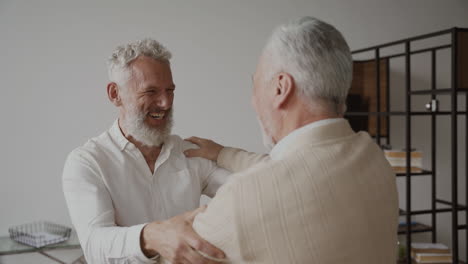 Two-Happy-Senior-Men-Friends-Greeting-Each-Other-With-A-Hug-And-Laughing-At-Home-2