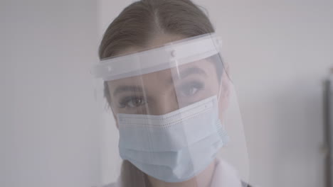 Rothaarige-Ärztin-Im-Weißen-Kittel-Mit-Medizinischer-Maske-Und-Gesichtsschutz,-Die-In-Die-Kamera-Schaut-1