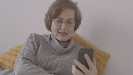 Anciana-Con-Anteojos-Sentada-En-La-Cama-Haciendo-Una-Videollamada-En-Un-Smartphone-1