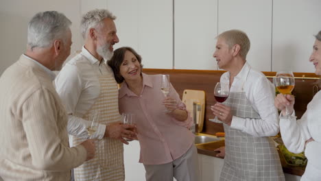 Gruppe-Fröhlicher-älterer-Freunde,-Die-Reden-Und-Lachen,-Während-Sie-Wein-In-Der-Küche-Trinken