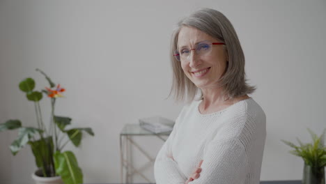 Senior-Woman-With-Gray-Hair-And-White-Shirt-Looking-At-Camera-Smiling-And-Putting-On-Eyeglasses