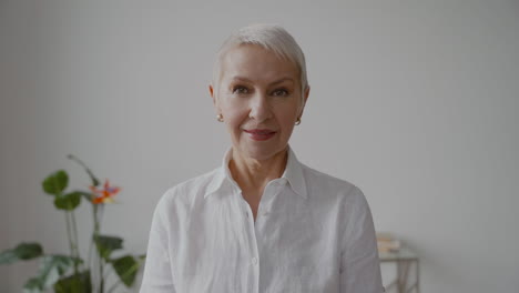 Senior-Woman-With-Short-White-Hair-And-White-Shirt-Looking-At-Camera-With-Serious-Expression