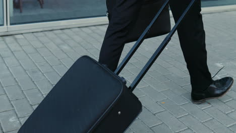 Close-Up-Of-The-Black-Suitcase-Wheeling-Behind-The-Businessman-In-The-Suit-While-He-Walking-The-Street
