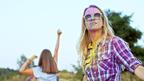 Young-Blond-Attractive-And-Happy-Woman-In-Sunglasses-Jumping,-Dancing-And-Having-Fun-With-Mixed-Races-Friends-Outdoor-At-The-Celebration-Of-Holi-Holiday