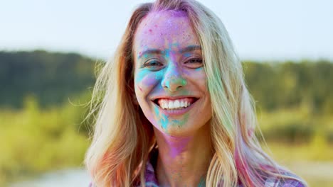 Portrait-Of-The-Blonde-Young-And-Beautiful-Woman-Looking-Straight-To-The-Camera-And-Smiling-Cheerfully-While-Being-In-Colorful-Spots-Of-Paints-Outside