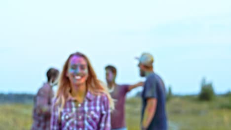 Blurred-Shot-Of-The-Young-People-Dancing-And-Having-Fun-Outdoors-At-The-Holi-Festival,-Blond-Girl-Coming-Closer-To-Camera,-Smiling-And-Posing-To-The-Camera