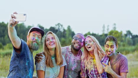 Gruppe-Junger,-Fröhlicher,-Multiethnischer-Männlicher-Und-Weiblicher-Freunde-In-Buntem-Farbpulver,-Die-In-Die-Smartphone-Kamera-Lächeln,-Während-Sie-Draußen-Beim-Holi-Fest-Ein-Selfie-Foto-Machen