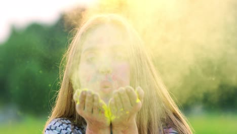 Portrait-Shot-Of-The-Young-Beautiful-Girl-Blowing-Paint-Powder-From-Hands-Palms-And-Smiling-To-The-Camera-Cheerfully-Outside