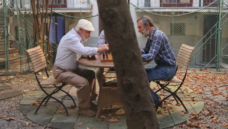 Three-Old-Men-Sitting-Outdoor-At-The-Table-And-Playing-Chess-At-The-Fresh-Air