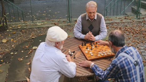 Draufsicht-Auf-Die-Drei-Grauhaarigen-Großväter,-Die-Bei-Einem-Schachspiel-Um-Den-Tisch-Sitzen-Und-Sich-Unterhalten