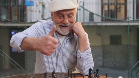 Close-Up-Of-The-Old-Retired-And-Smiled-Man-Moving-A-Chessman-On-The-Board-And-Giving-His-Thumb-Up