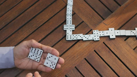 Draufsicht-Dominospiel-Auf-Dem-Holztisch-Und-Alte-Hände,-Die-Spielen-Und-An-Der-Reihe-Sind