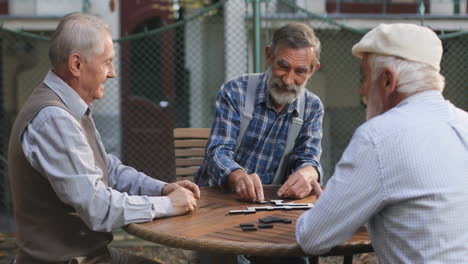 Cheerful-Old-Men-Playing-A-Domino-Game-At-The-Fresh-Air-And-One-Of-Them-Winning