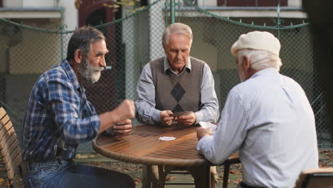 Old-Best-Friends-Playing-Cards-Game-At-The-Fresh-Air-And-Making-Their-Turns-On-The-Wooden-Table