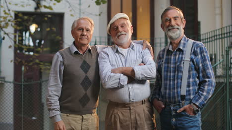 Portrait-Shot-Of-The-Three-Senior-Men-Friends-Standing-And-Smiling-To-The-Camera-In-Front-Of-The-Camera-In-The-Yard