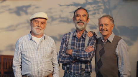 Three-Retired-Old-Men-Best-Friends-Standing-At-The-Wall-Outdoor,-Looking-At-The-Camera-And-Smiling