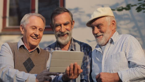 Portrait-Shot-Of-The-Three-Old-Retired-Grandfathers-Talking-While-Watching-Something-On-The-Tablet-Device