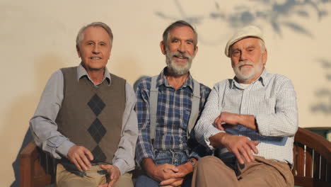 Drei-ältere-Männer-Ruhen-Sich-Auf-Einer-Bank-Aus-Und-Lächeln-In-Die-Kamera-An-Der-Wand