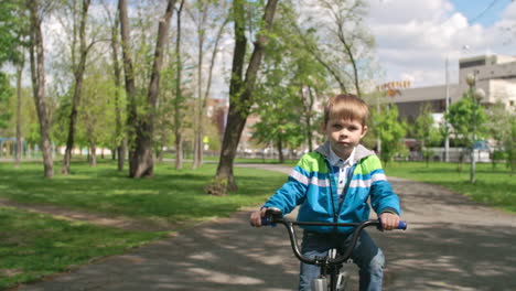 Blond-Boy-In-Sweatshirt-And-Jeans-Riding-A-Bike-In-The-Park-1