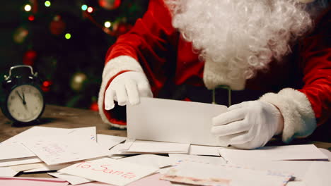 Der-Weihnachtsmann-Liest-Einen-Brief,-Der-An-Einem-Tisch-In-Einem-Raum-Mit-Weihnachtsdekoration-Sitzt