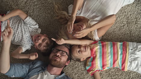 Top-View-Of-Father-And-Mother-And-Two-Children-Lying-On-The-Floor-With-Their-Heads-Together-And-Playing-With-The-Index-Finger