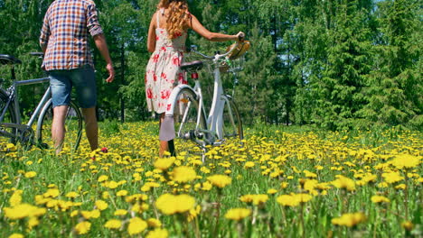 Woman-And-Man-Wear-Confortable-Clothes,-They-Carry-A-Bicycle-Walking-In-The-Meadow