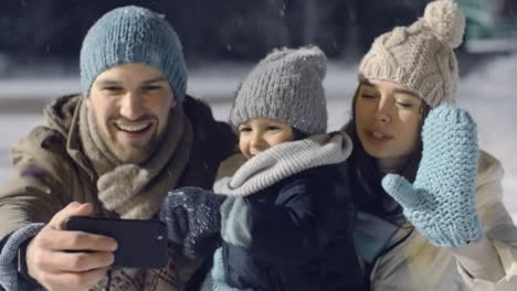 Couple-With-Their-Son-In-Winter-Clothes-Making-A-Video-Call-In-The-Park-While-It-Snows