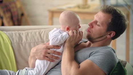 Father-Lying-On-The-Sofa-Holding-His-Baby-And-Showing-Him-Affection