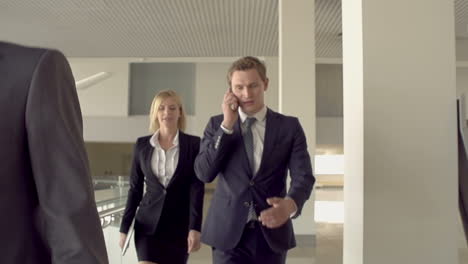 Businessmen-And-Businesswoman-Walking-Around-The-Office,-One-Of-Them-Talking-On-The-Phone-Accompanied-By-A-Blonde-Woman